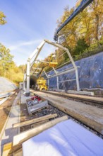 Crane lifts construction material for a tunnel surrounded by autumnal forest and blue skies,