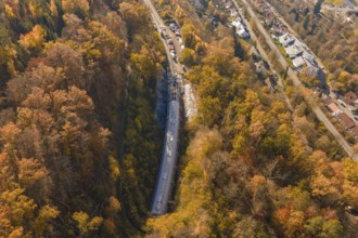 Aerial view of a construction site in colorful autumn forest with adjacent roads and houses,