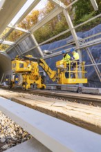 Two workers operate yellow machines in a partially built metal structure, Hermann Hesse Railway Bat