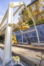 Construction workers erect a metal structure on rails along a wooded area, Hermann Hesse Railway