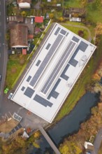 Building with solar roof, surrounded by a village and river, viewed from the air in an autumn