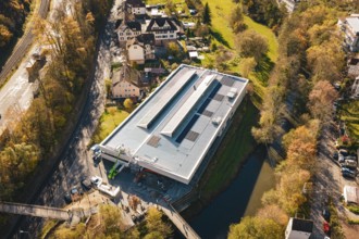 Bird's eye view of a modern building with solar cells, nestled in an autumnal village and river