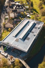 Aerial view of a modern building with solar panels on the roof, surrounded by an idyllic village