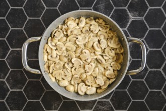 Sliced mushrooms are being fried in a large pan, giving off a savoury aroma. The scene is set on a