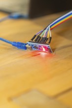 Red glowing circuit board connected to USB cable on wooden table, Jugend Forschungszentrum Nagold,
