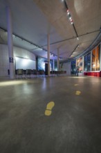 Large, modern room with yellow footprints on the floor and lighting on the ceiling, Amazonia