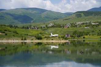 Lakeside village with mountains in the background, calm water with reflection, Tu-134A aircraft as