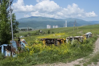 Rusty vehicles stand in a meadow in front of a wooded mountain panorama, scrap cars serve as a
