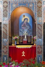 Religious altar with icon and candles richly decorated with flowers in a decorated wall niche,