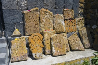 Historical, engraved stones with flowers on concrete in front of a wall, cross stones at Sevanavank