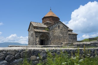 Historic stone church with orange roof against blue sky and white clouds, Sevanavank Monastery,