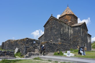 Visitors in front of a historic stone monastery under clear skies, Sevanavank Monastery, Sevan
