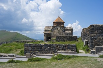 A small stone monastery stands amidst a green landscape under a blue sky, Sevanavank Monastery,