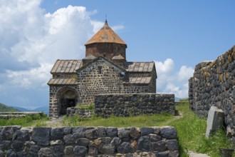 Front view of a historic stone church with brick wall and overgrown landscape, Sevanavank