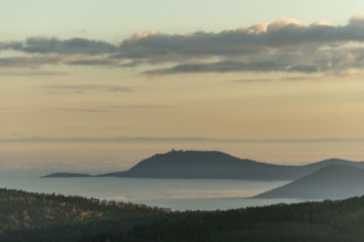 The landscape of hills and mountains is illuminated by a gentle sunset. Sea of fog in distance