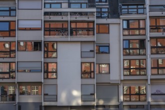 The building has bare facades with numerous balconies. The windows reflect sunlight and create a