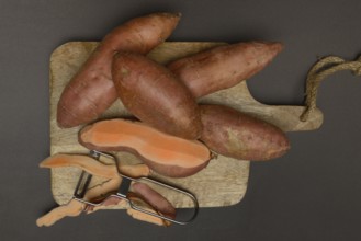 Sweet potatoes with potato peeler on wooden board, Ipomoea batatas