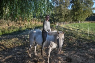 Young girl sitting on her white mare under a willow (Salix), Othenstorf, Mecklenburg-Western