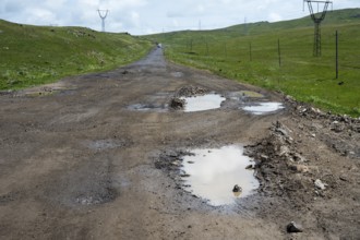 Unpaved road with potholes surrounded by green hills and power lines, M10 near Geghovit,