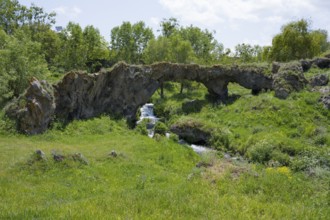 Scene with a natural rock arch and a small waterfall in green surroundings, Tsakkar Bridge in the