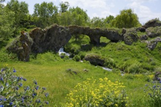 Landscape with natural rock arch, green vegetation and flowing stream, Tsakkar bridge in the