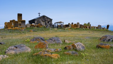 Small chapel surrounded by old tombstones on a hilly meadow under a blue sky, khachkar at the