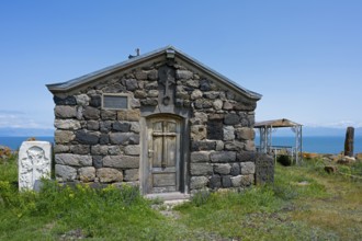 Stone chapel with wooden door in the foreground, sea in the background under clear sky, Chapel of