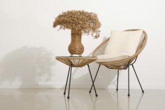 A modern space features a rattan chair with a soft pillow beside a small table. A woven vase filled