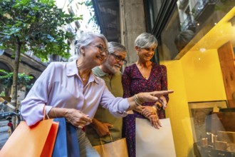 Three happy senior friends, two women and one man, standing on a city street, carrying shopping