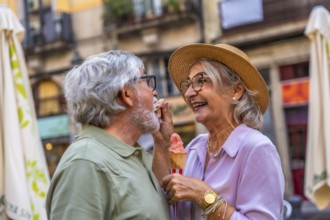 Happy senior couple enjoying a sweet treat together, with the woman playfully feeding her husband