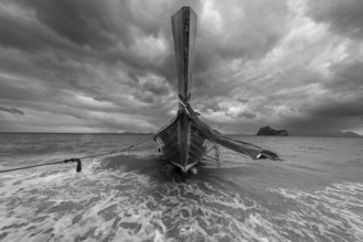 Longtail boat on the beach with dark rain clouds behind it, Koh Ngai island, Andaman Sea, Satun
