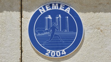 Blue sign with ancient columns and a runner in front of a stone wall, Ancient Stadium, Nemea,