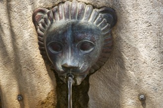 A bronze lion head sculpture that serves as a fountain and steers water in an ancient setting,