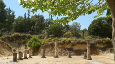 Ancient ruins with multiple pillars nestled in a lush green landscape under cloudy sky, Ancient