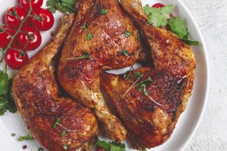 Grilled fried chicken legs, served, with fresh cherry tomatoes, and herbs, on a white plate,