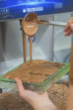 Hand pouring warm chocolate from a ladle into chocolate molds, Christmas baking, Haselstaller Hof,