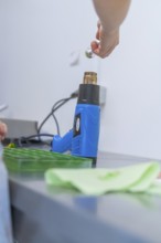 Person uses a blue heat gun to process green objects on a workbench, Weihnachtsbacken, Haselstaller