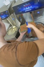 Person uses a blue tool to fill chocolate into a mold at a tempering machine, Christmas baking,