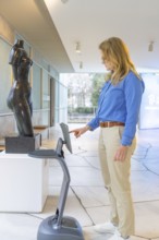 Woman interacting with a device in front of a statue in a modern setting, robotic personality