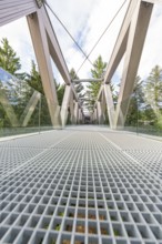 Architecturally impressive metal and wood bridge with glass railing against a wooded background,