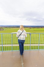Woman looking out over an extensive green field from the tower, DÃ¼rrenmettstetten observation