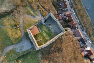 Aerial view of a castle ruins with adjacent streets and houses, surrounded by autumn light,
