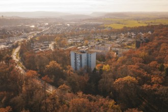 A residential building towers over an autumnal forest with a town behind it, MÃ¼hlacker, Enzkreis,