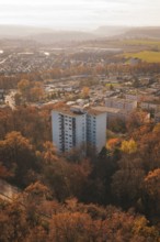 A high-rise residential building rises between autumn trees in an urban area, MÃ¼hlacker, Enzkreis,