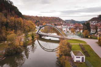Beautiful bridge in autumn landscape, framed by colorful trees and reflected in water, Sulz am
