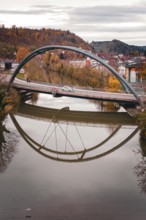 Bridge with arched design reflecting in calm river water surrounded by autumn trees, Sulz am