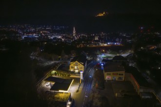 Nighttime view of city with illuminated gas station and distant castle on hill, Nagold, Calw