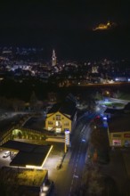 Nighttime city view with illuminated gas station, castle on hill in the distance, Nagold, Calw