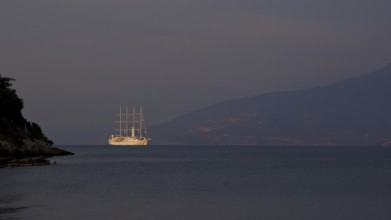 A large sailing ship sails in the calm sea in front of a dark mountain silhouette, Nauplion,