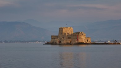 Bourtzi island fortress, a historic castle island in calm water against a mountain backdrop,